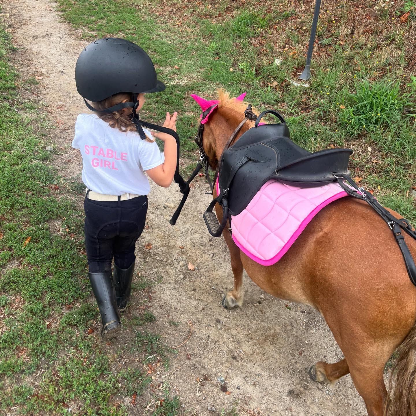 Un bambino in tenuta da equitazione conduce un pony con una sottosella rosa su un sentiero sterrato.