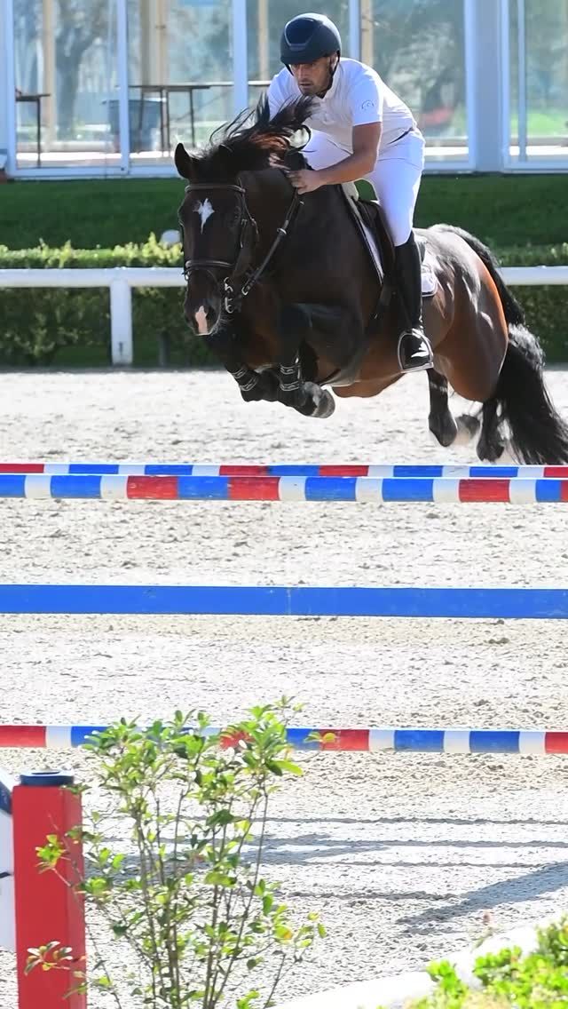 Un uomo a cavallo salta una recinzione a strisce blu e bianche durante una gara all'aperto.