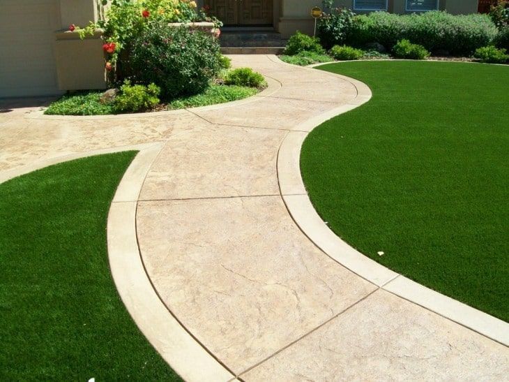 A concrete walkway leading to a house with artificial grass