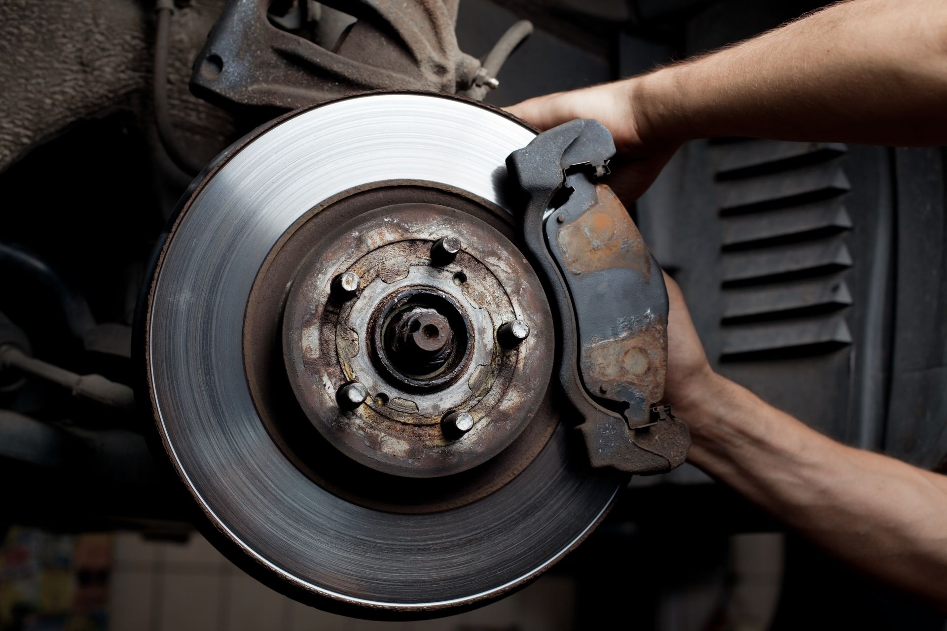 Hands working on car brake disc and caliper.