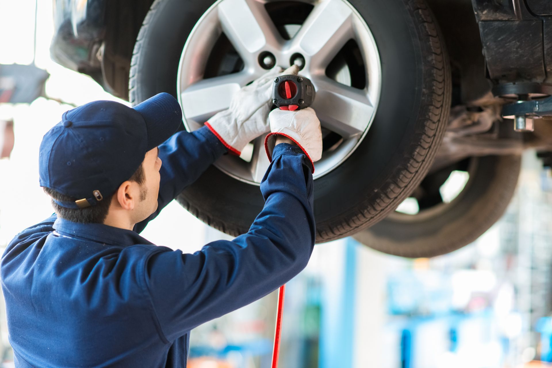 Mechanic removing a car tire with an impact wrench, working in a repair shop.