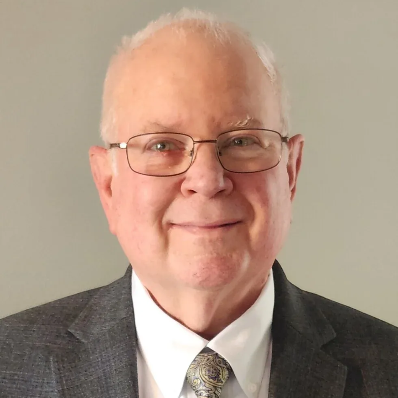Man wearing glasses and suit smiling.