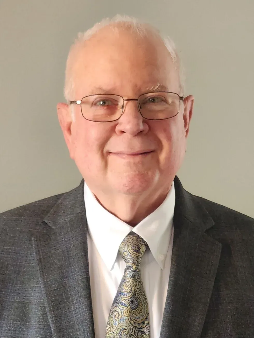 Man wearing glasses, gray suit jacket, patterned tie, smiling.
