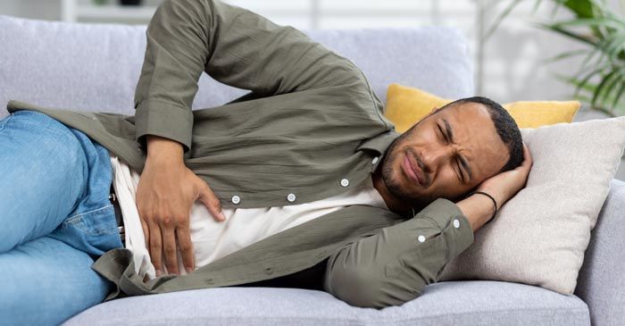 Man lying on a couch holding his stomach, appearing to be in pain, needing Digestive Disorder Remedies - Dr. Louis Granire,r Holistic Chiropractor