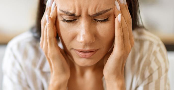 Woman with closed eyes, holding temples, appears to be experiencing a headache, indoors. Headache Remedies - Dr. Louis Granirer Holistic Chiropractor