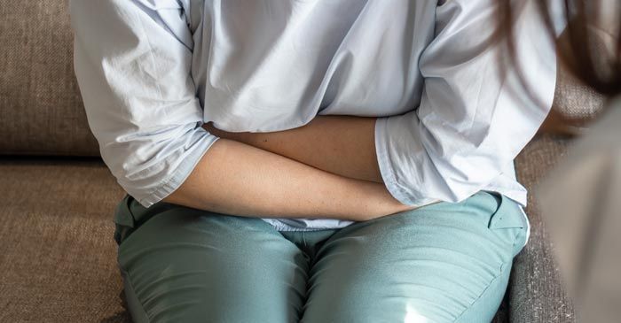Person clutching stomach, possibly in pain, while seated suggesting the need for Irritable Bowel Syndrome Remedies - Dr. Louis Granirer Holistic Chiropractor