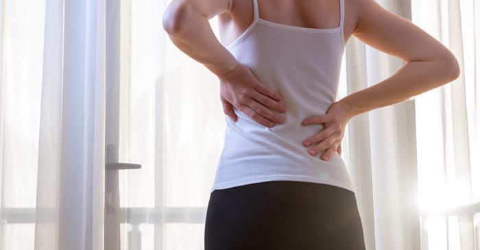 Woman in white tank top, holding her lower back, appears to be in pain. needing Pinched Nerve Treatments - Dr. Louis Granirer Holistic Chiropractor