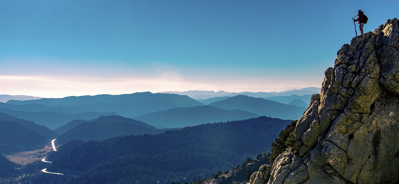 Person stading on a mountain overlooking a valley below