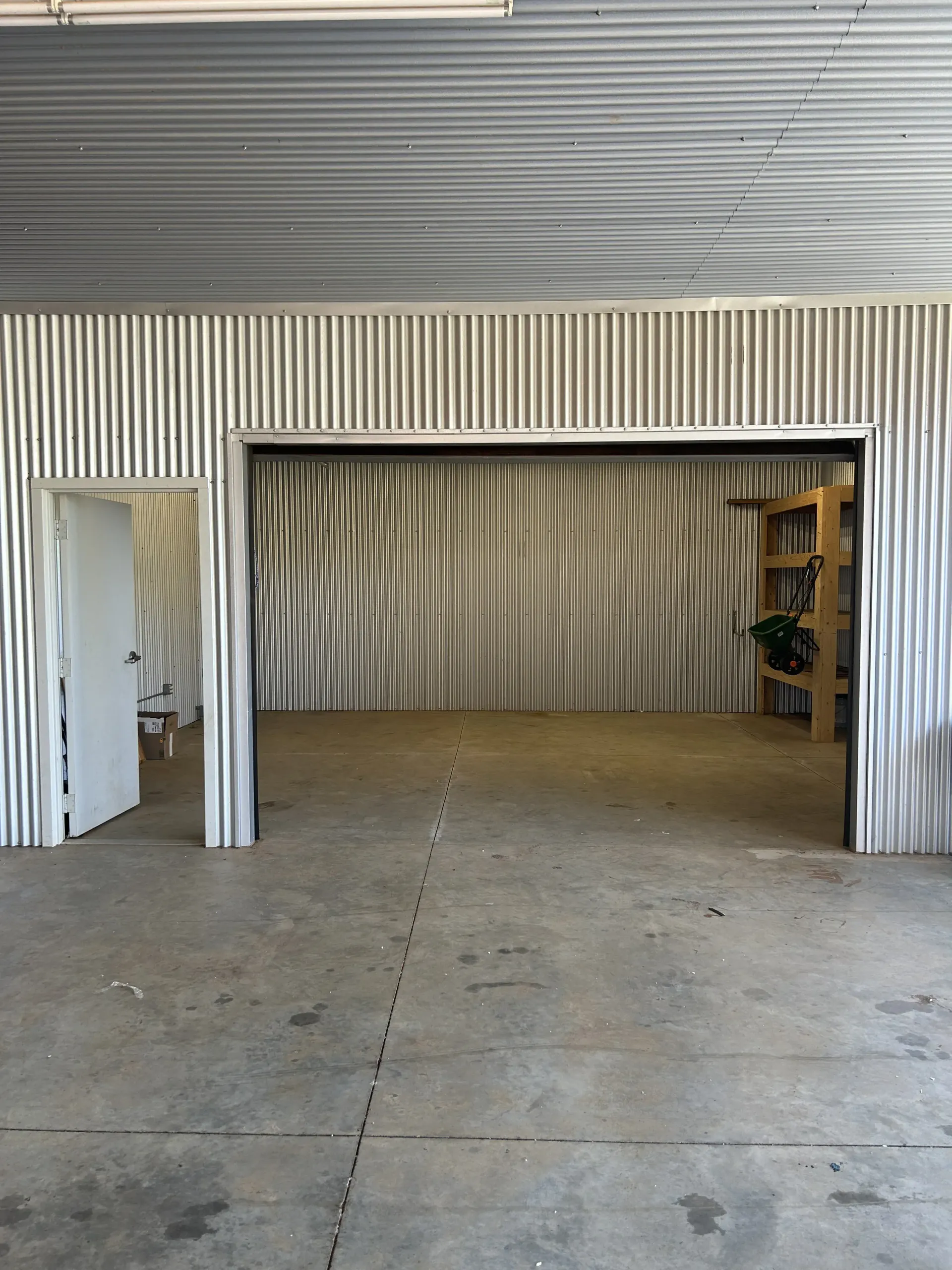 Empty warehouse interior with corrugated metal walls, concrete floor, and open doorway to a smaller room