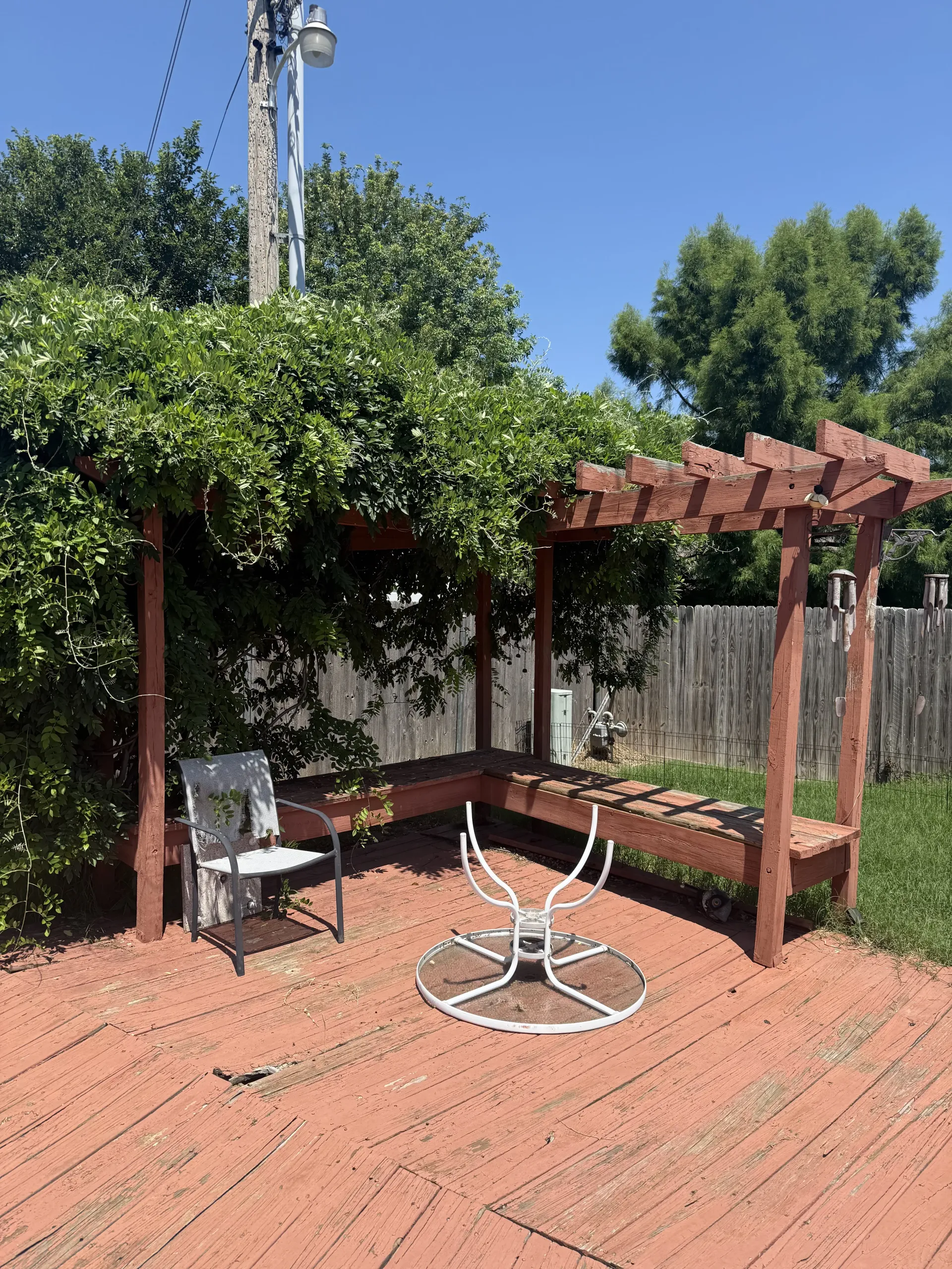 Backyard patio with red brick pavers, pergola, metal table and chairs, and leafy green trees.