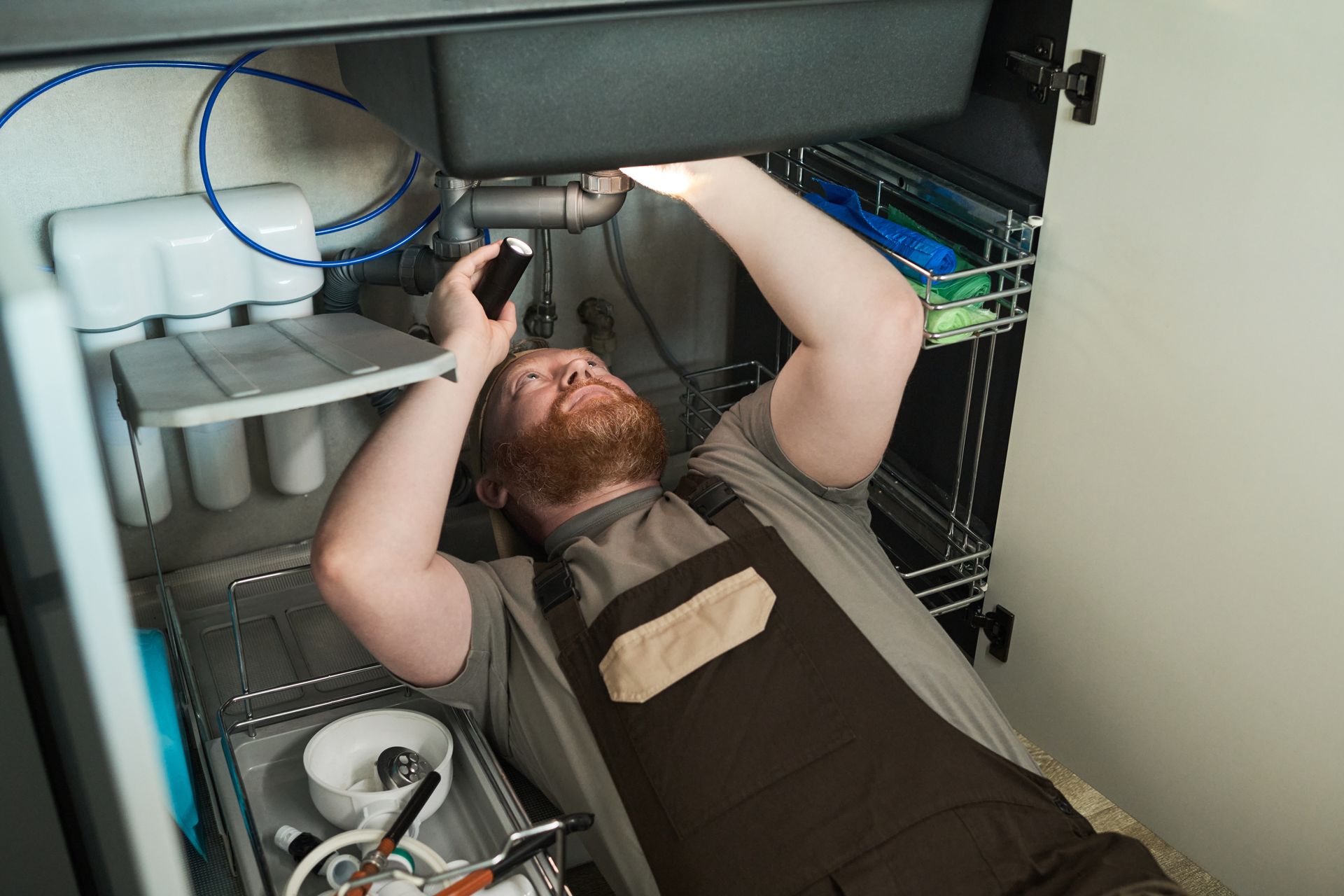 A plumber is performing affordable plumbing services under the sink, repairing the plumbing system.