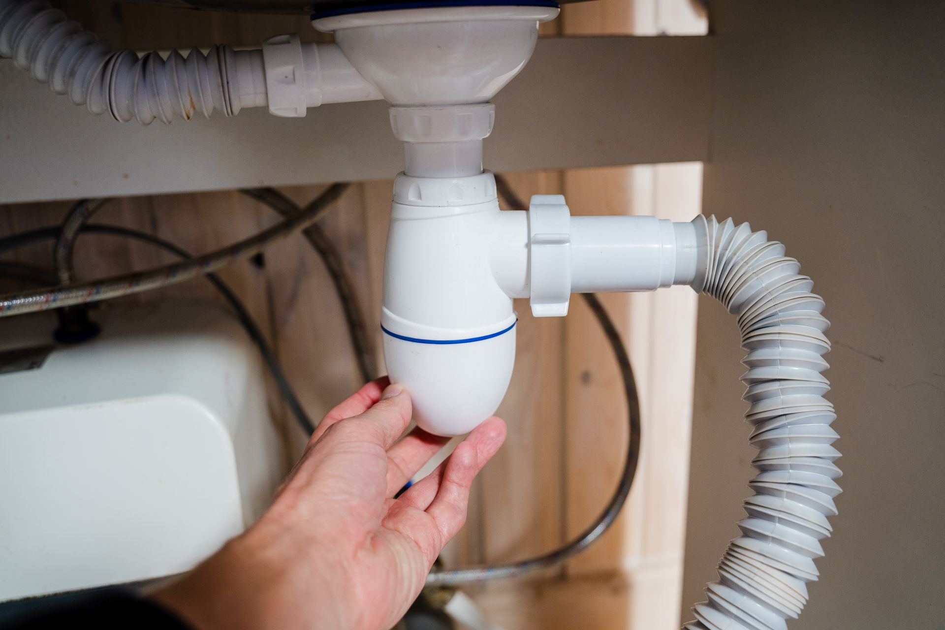 A close-up of a plumber adjusting a white PVC pipe fitting under a kitchen sink after-hours.