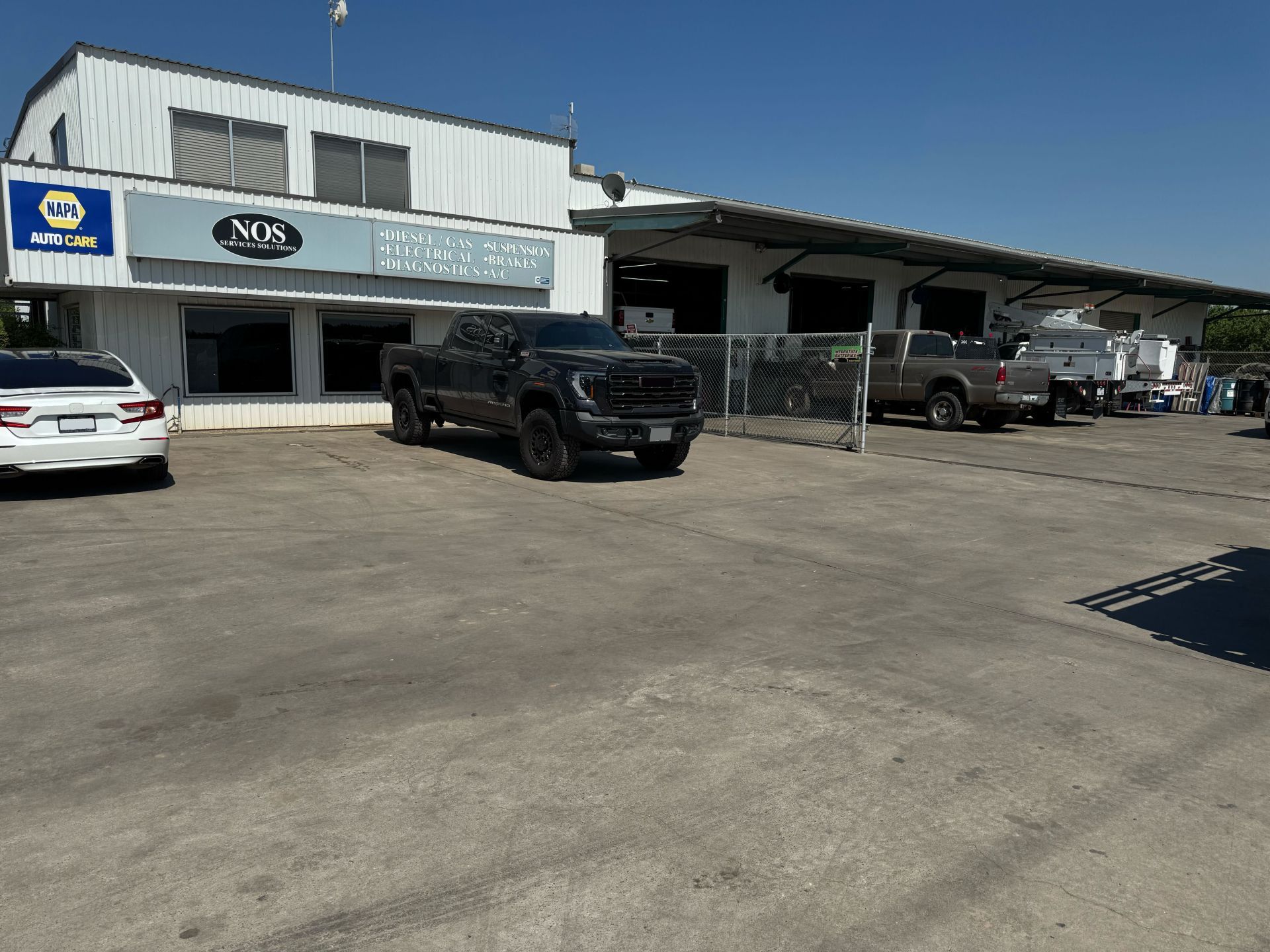 Mechanic in a shop works on a vehicle engine, wearing safety glasses and a dark blue shirt. | NOS Service Solutions