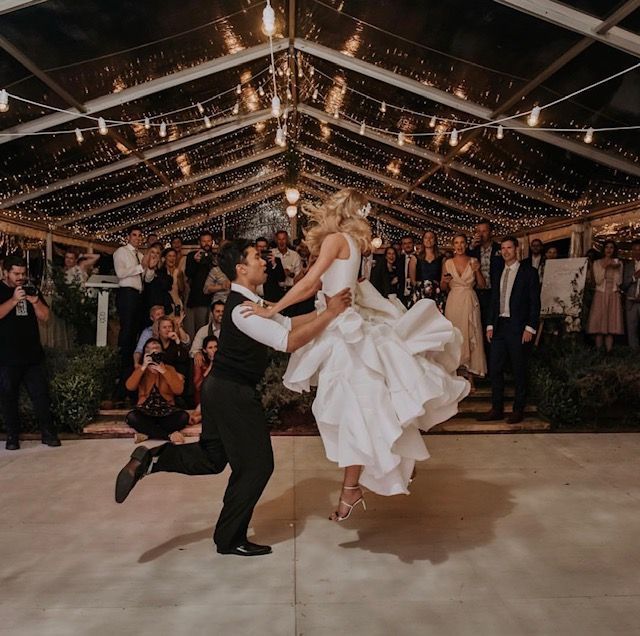 A bride and groom are dancing under a clear tent