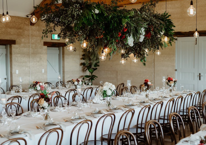 A long table set for a wedding reception with flowers hanging from the ceiling.