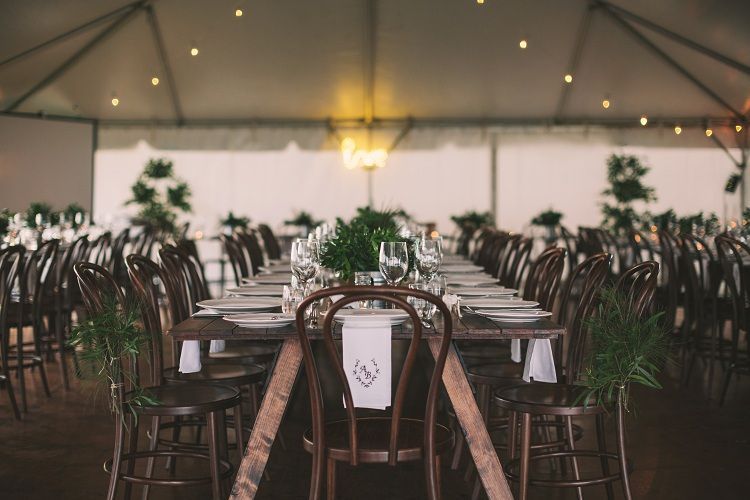 A long table with plates , glasses , and chairs under a tent.