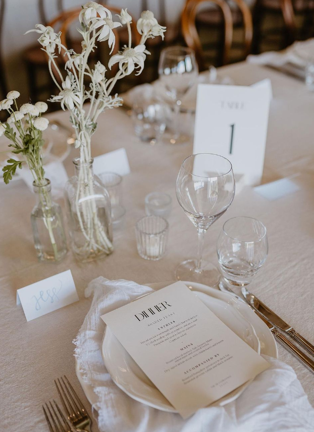A table set for a wedding reception with plates , glasses , and flowers.
