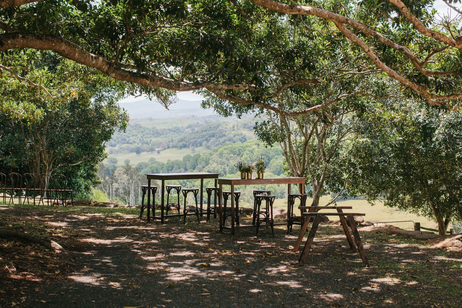 A picnic table and chairs under a tree with a view of a mountain.