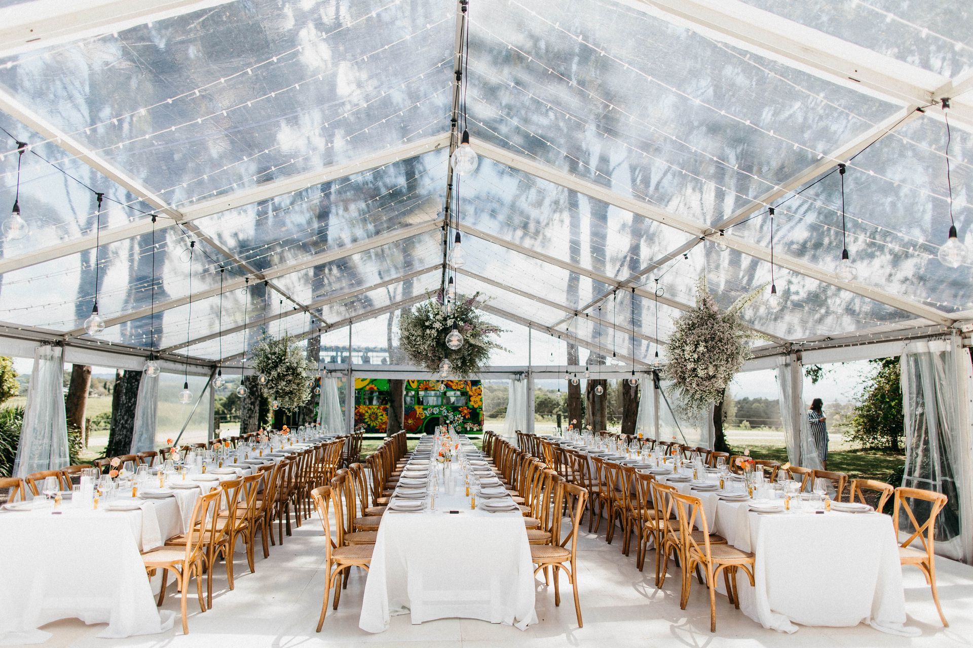 A large clear tent with tables and chairs set up for a wedding reception.