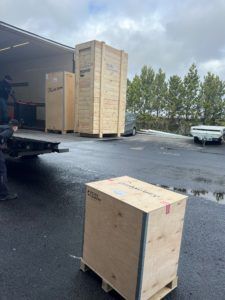 Afhending á trékössum úr vörubíl; maður við ramp; skýjað himinn.