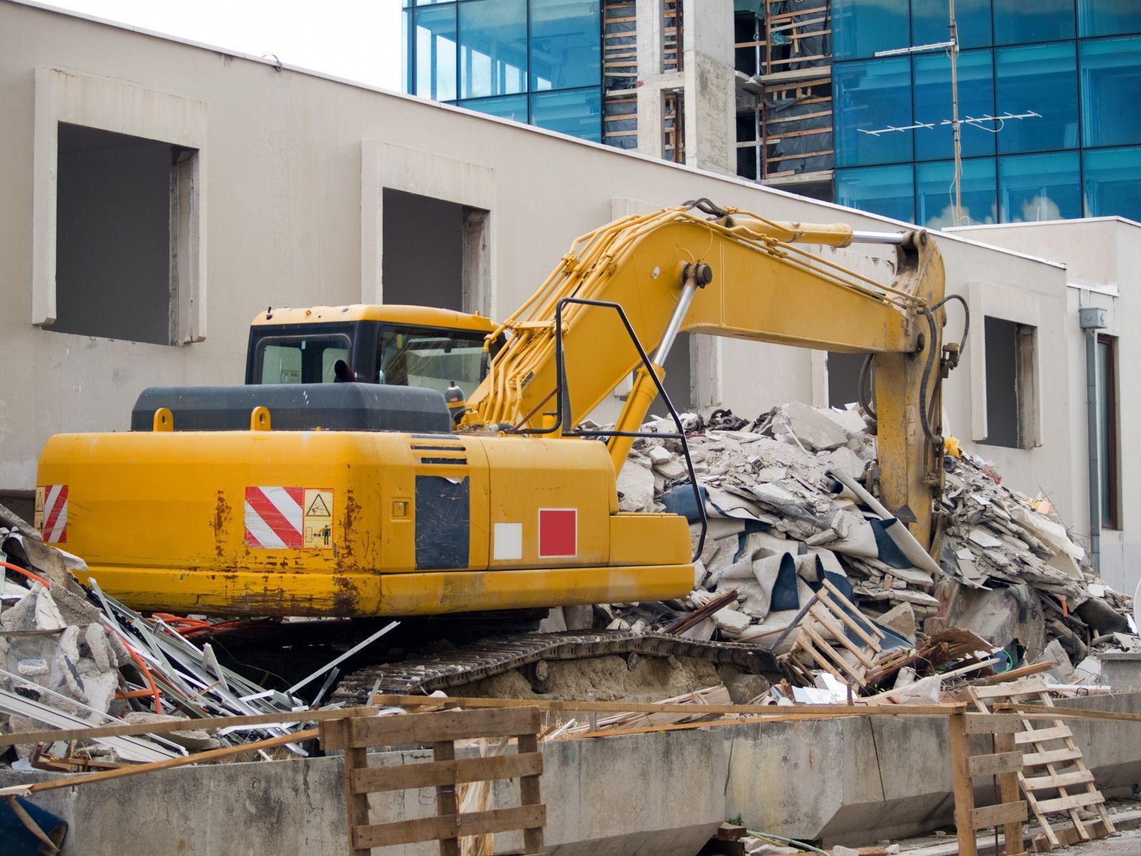 A yellow excavator is demolishing a building on a construction site.