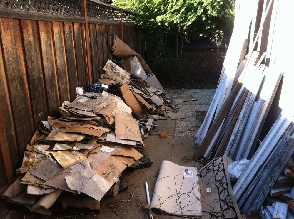 Pile of cardboard boxes and construction debris next to a wooden fence.