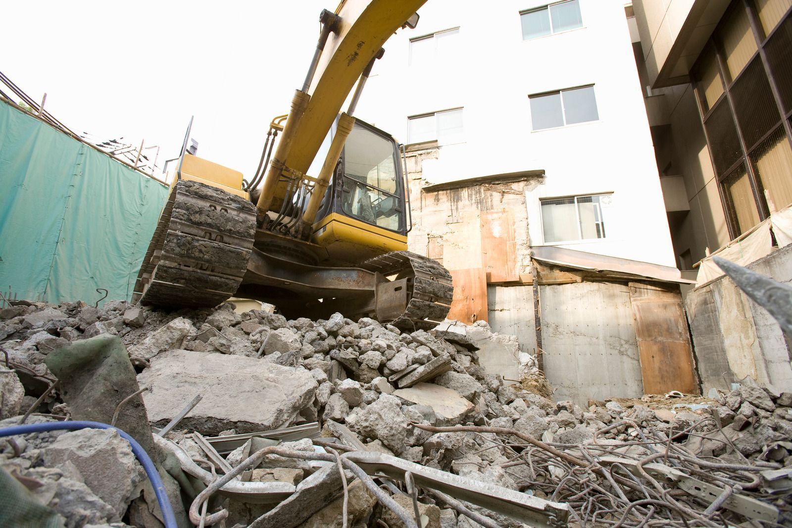 Yellow excavator demolishing building, surrounded by rubble and debris.
