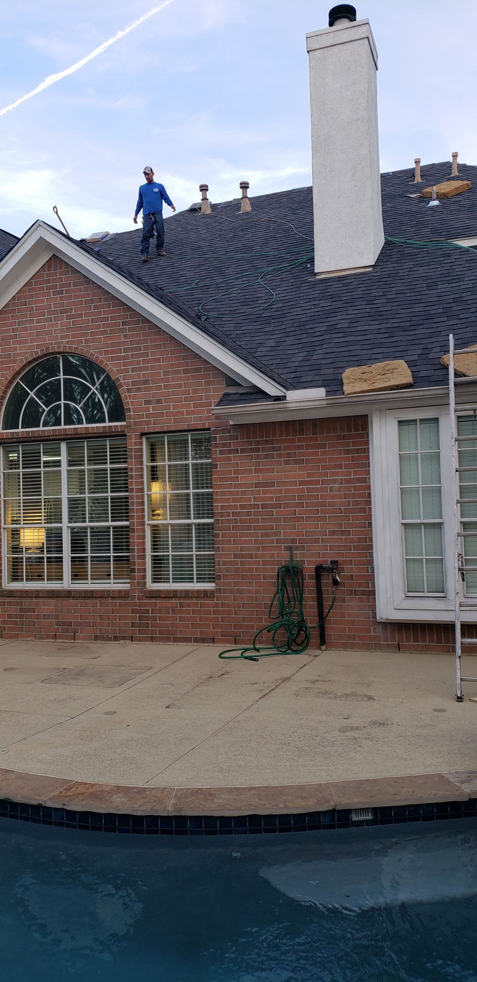 A man is standing on top of a roof next to a pool.