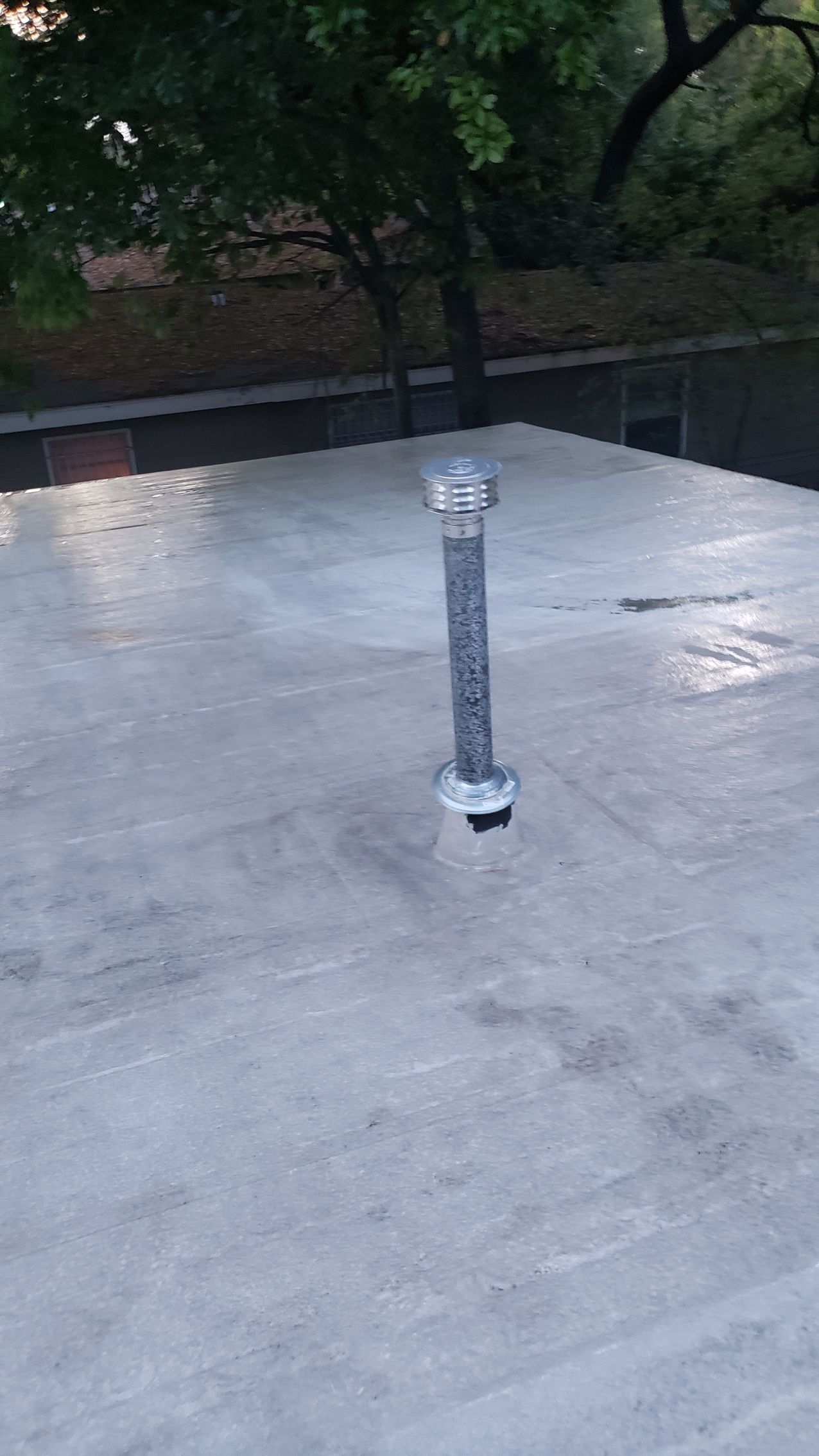 A roof with a pipe on it and trees in the background.