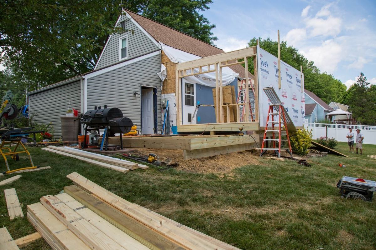 A house under construction, with wooden framing and a deck, on a grassy lawn.