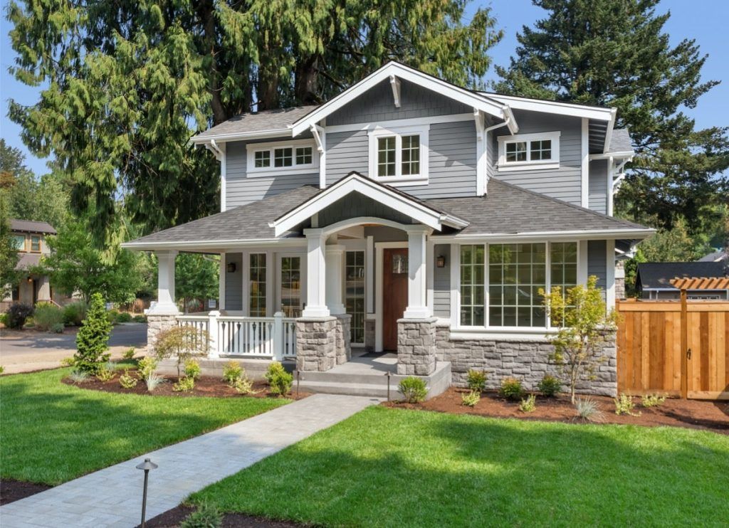 Gray Craftsman house with porch, stone accents, and green lawn on a sunny day.