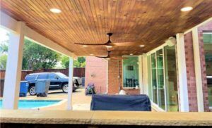 Outdoor patio with wood ceiling, fans, lights, pool, brick wall, and a vehicle.