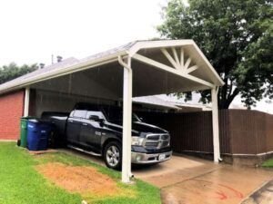 Black pickup truck parked under a white carport; green trash cans and a brown fence are visible.