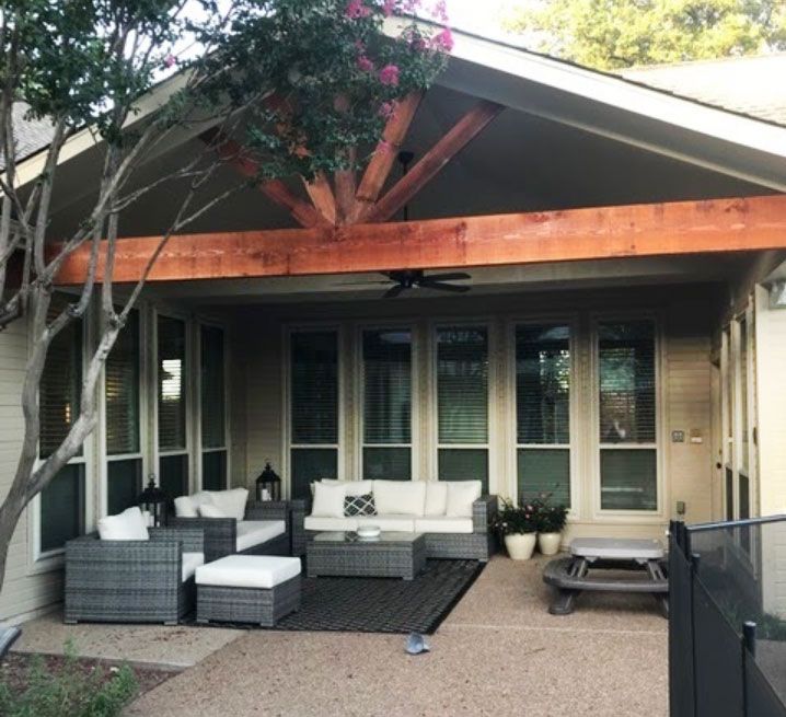 Patio with outdoor seating under a covered area with a wooden beam and a tree.