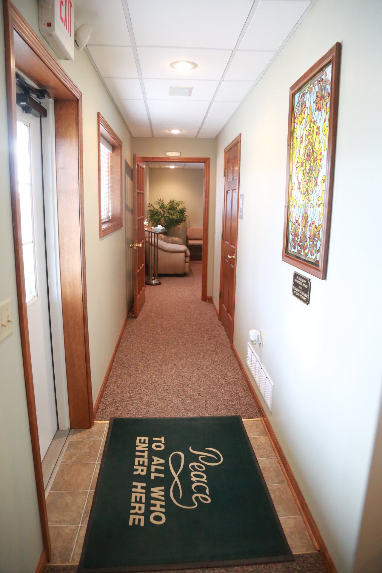A hallway with a green mat that says peace to all who enter here