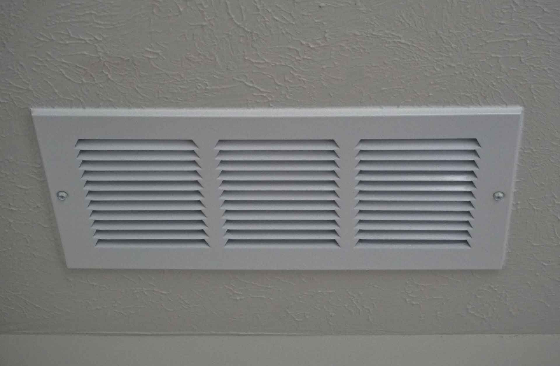 A white air vent is hanging from the ceiling of a room.