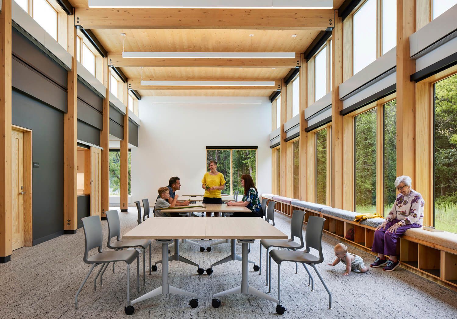 A Group of People Are Sitting at Tables in a Room With Lots of Windows.