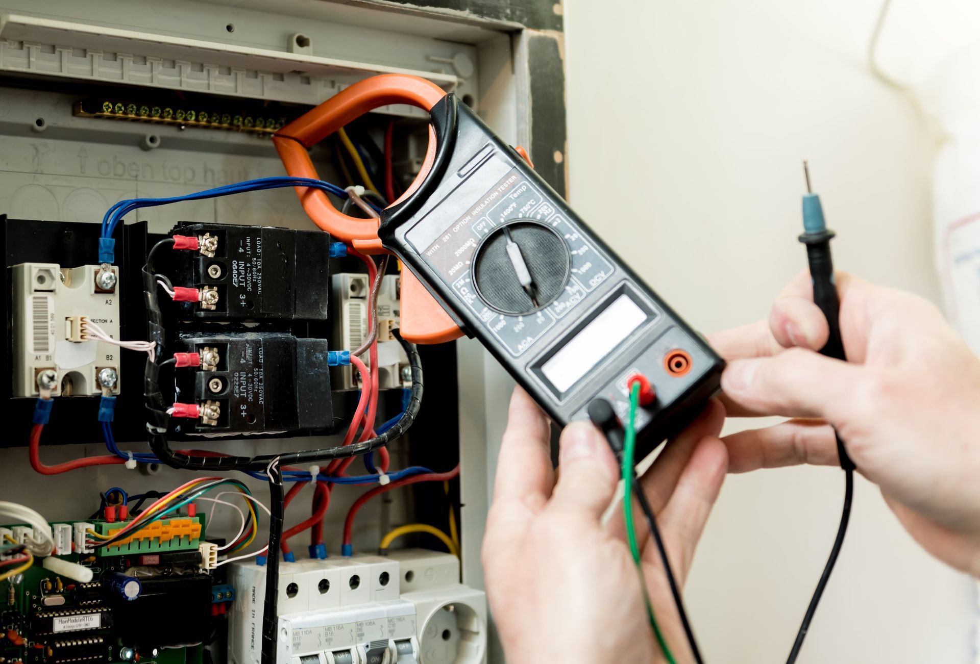 Electrician testing an open electrical panel with a multimeter and probe leads.