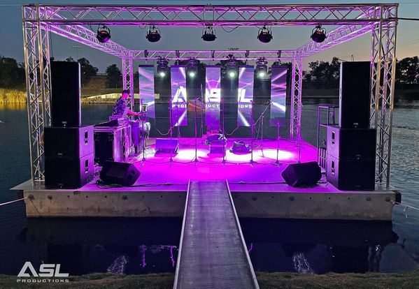 a stage with purple lights and speakers is floating on top of a body of water .