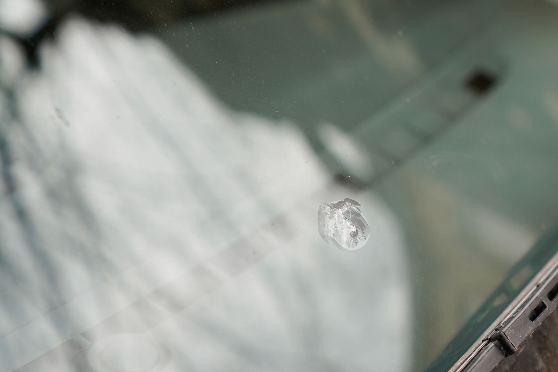 Broken gravel impact on car windshield damaged glass windscreen with trace of stone.