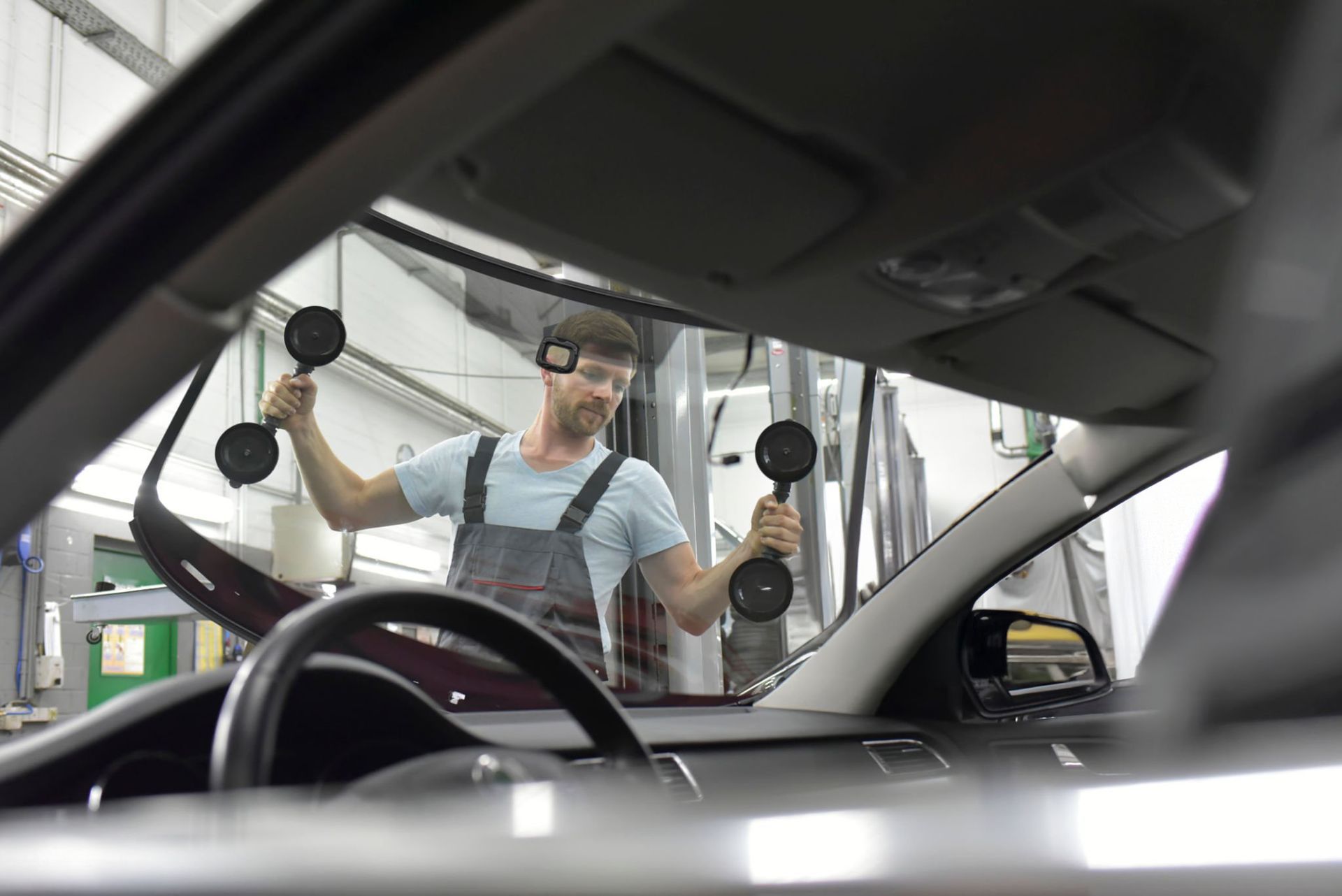Worker installing a windshield in a car at an auto repair shop.