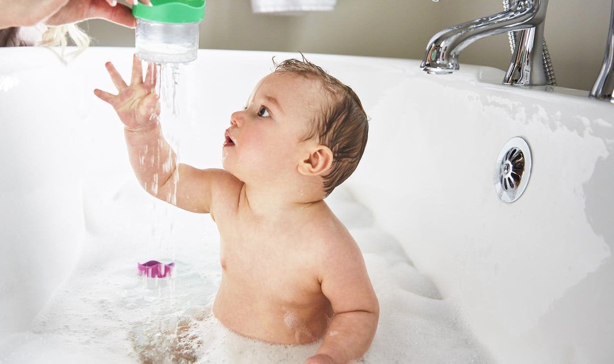 A baby is taking a bath in a bathtub and playing with water.