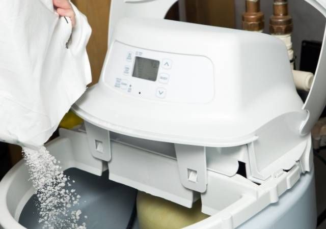 A person is pouring salt into a water softener