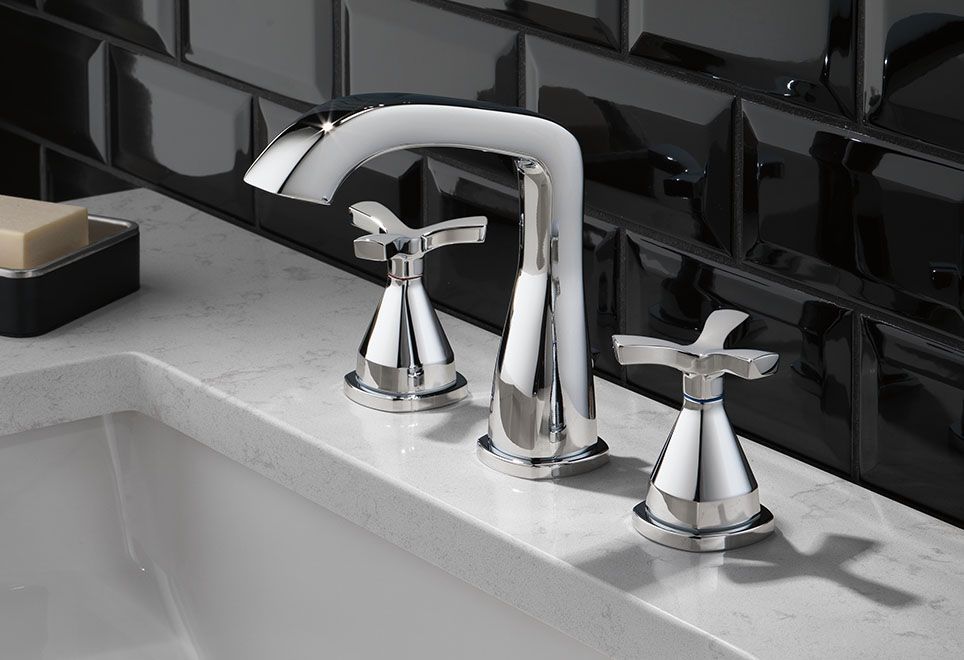 A bathroom sink with a chrome faucet and black tiles.