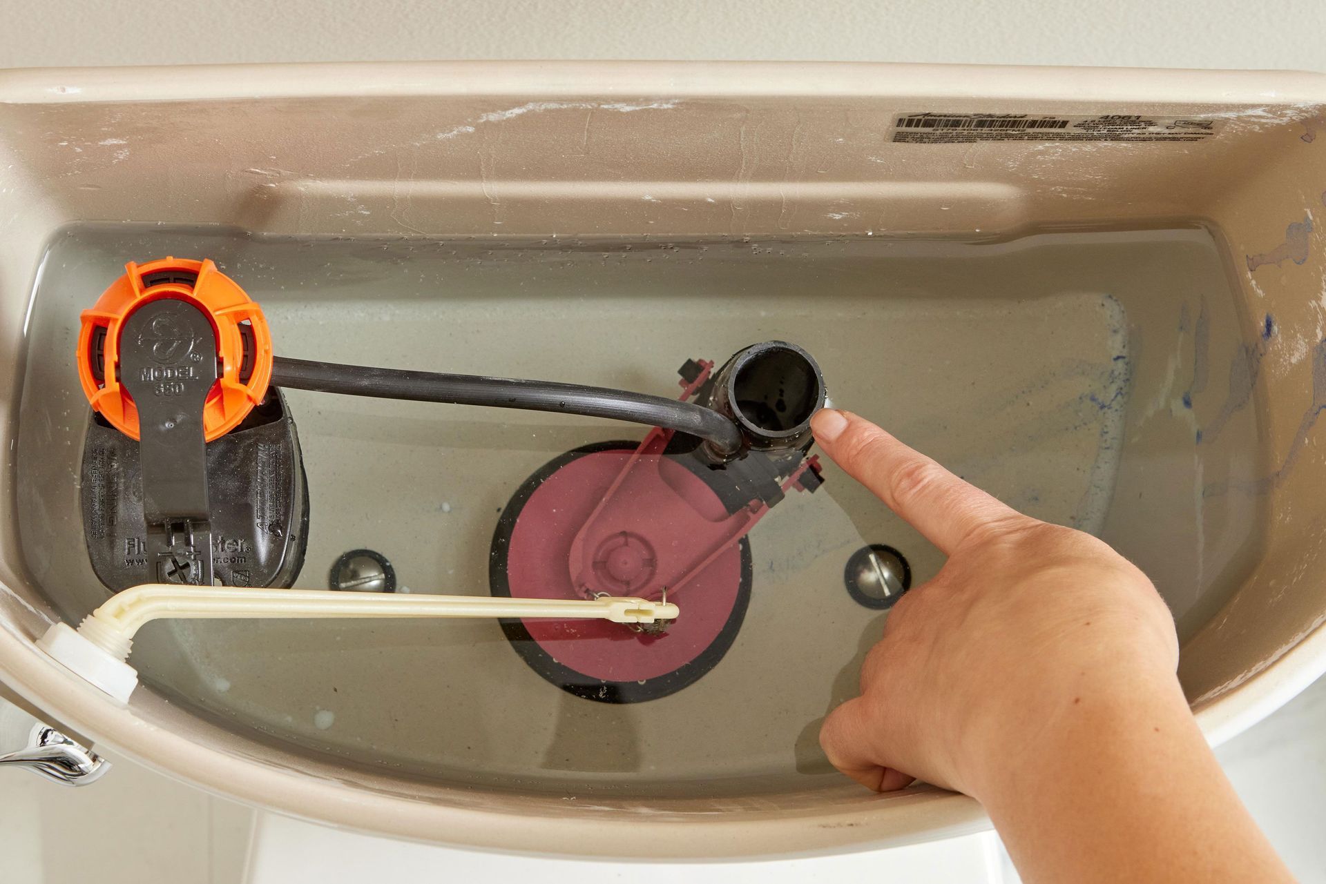 A person is pointing at a toilet tank with their finger.