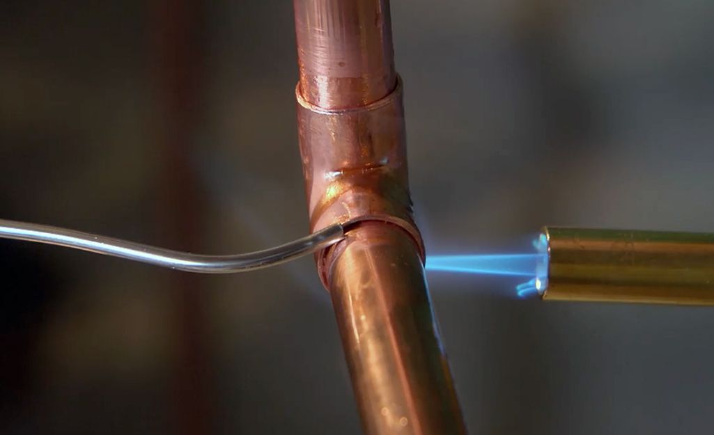 A person is welding a copper pipe with a torch.