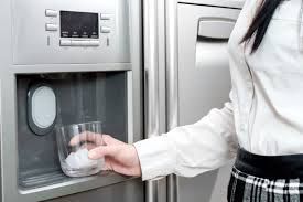 A woman is pouring ice into a glass from a refrigerator.