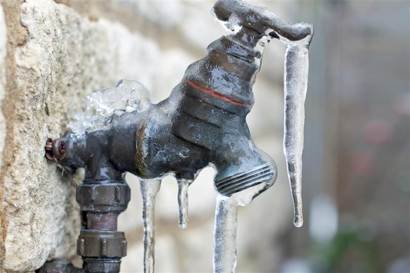 Frozen outdoor water faucet with icicles.
