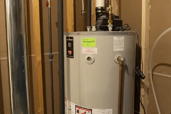 A water heater is sitting in a basement next to pipes.