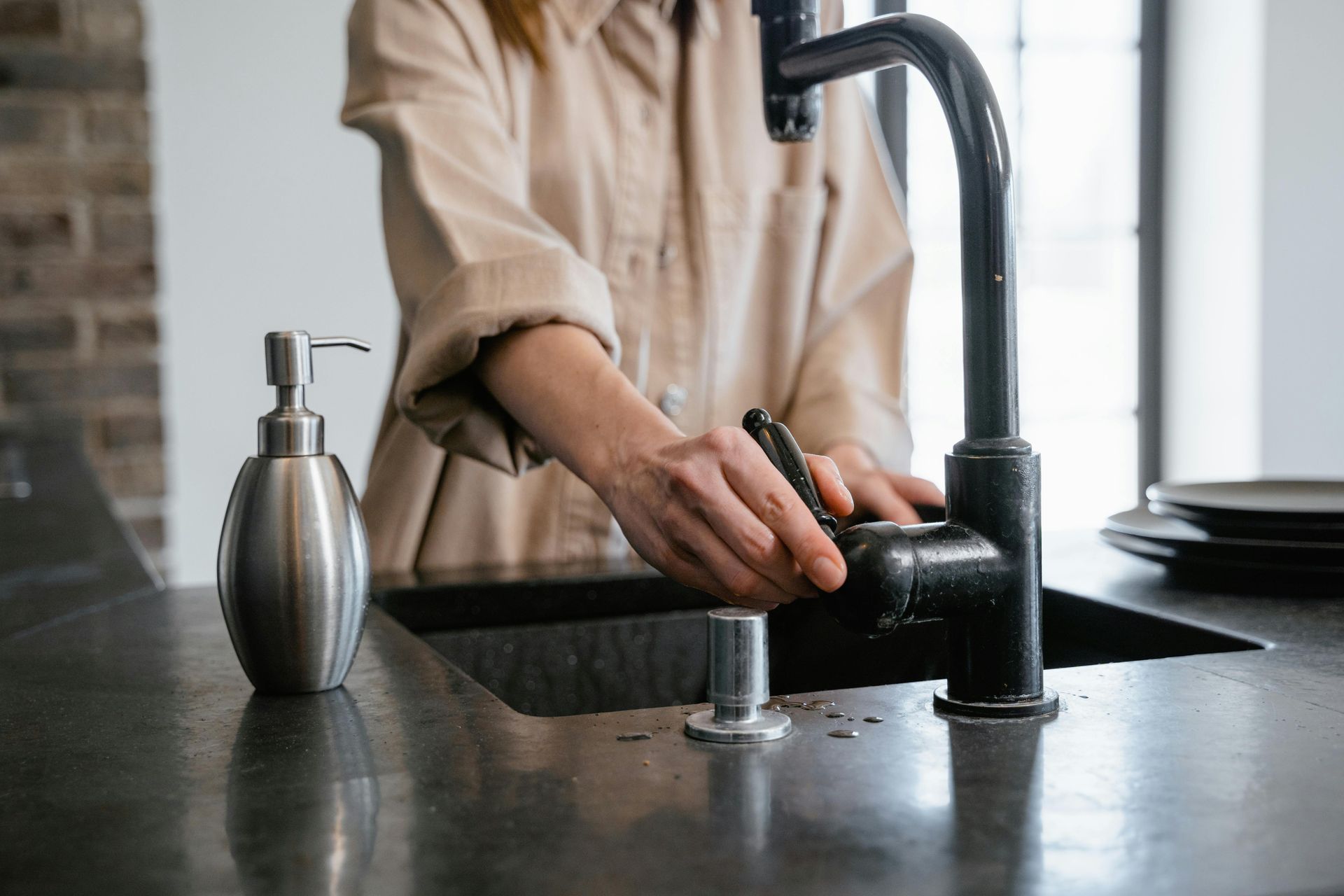 A woman is washing dishes in a kitchen sink.